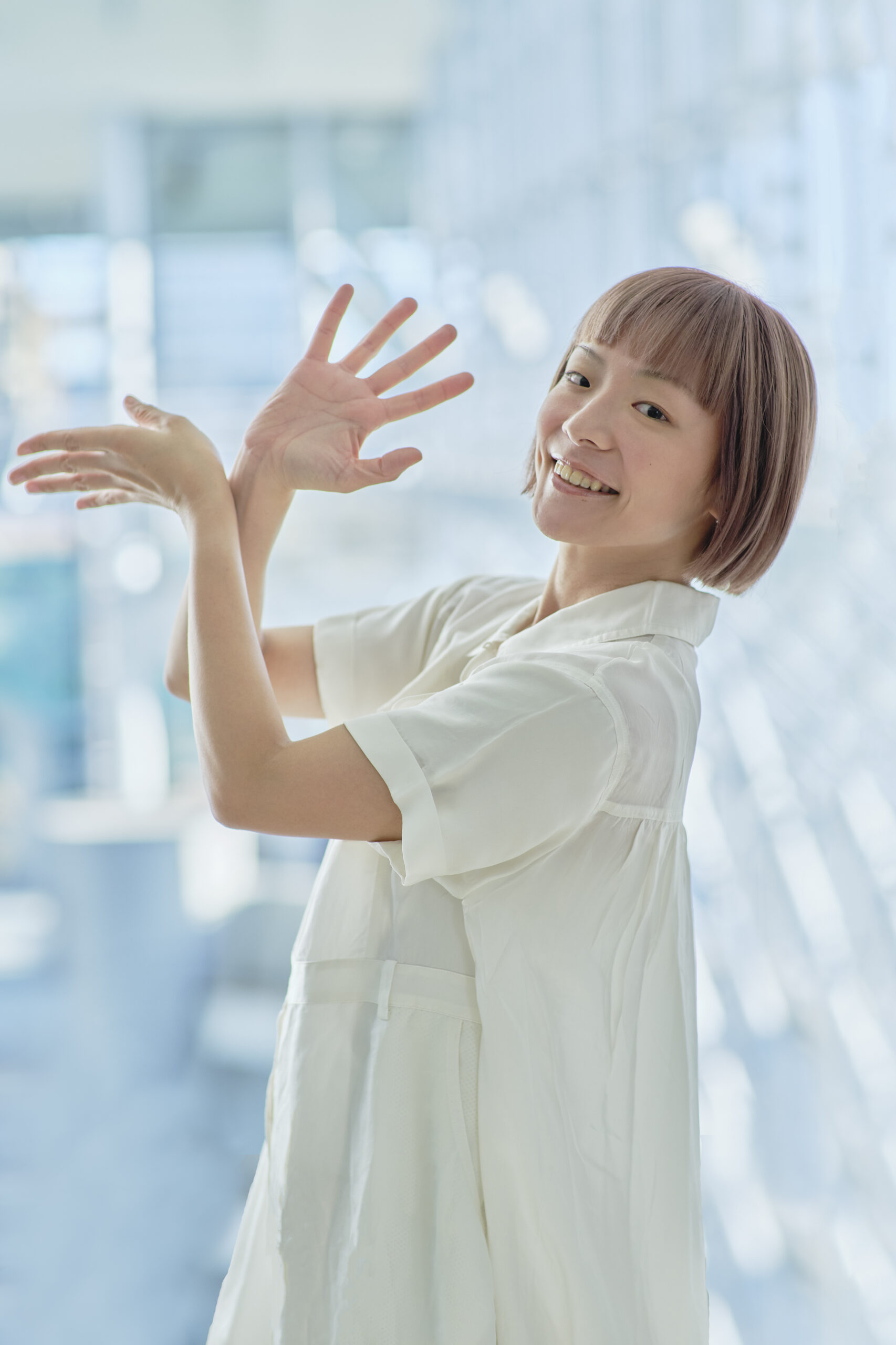 神奈川県あそび歌プロジェクト「世界の歌とあそぼう」振付家のホナガヨウコさんのアーティスト写真。身体は横向きのまま、笑顔をこちらに向けている。