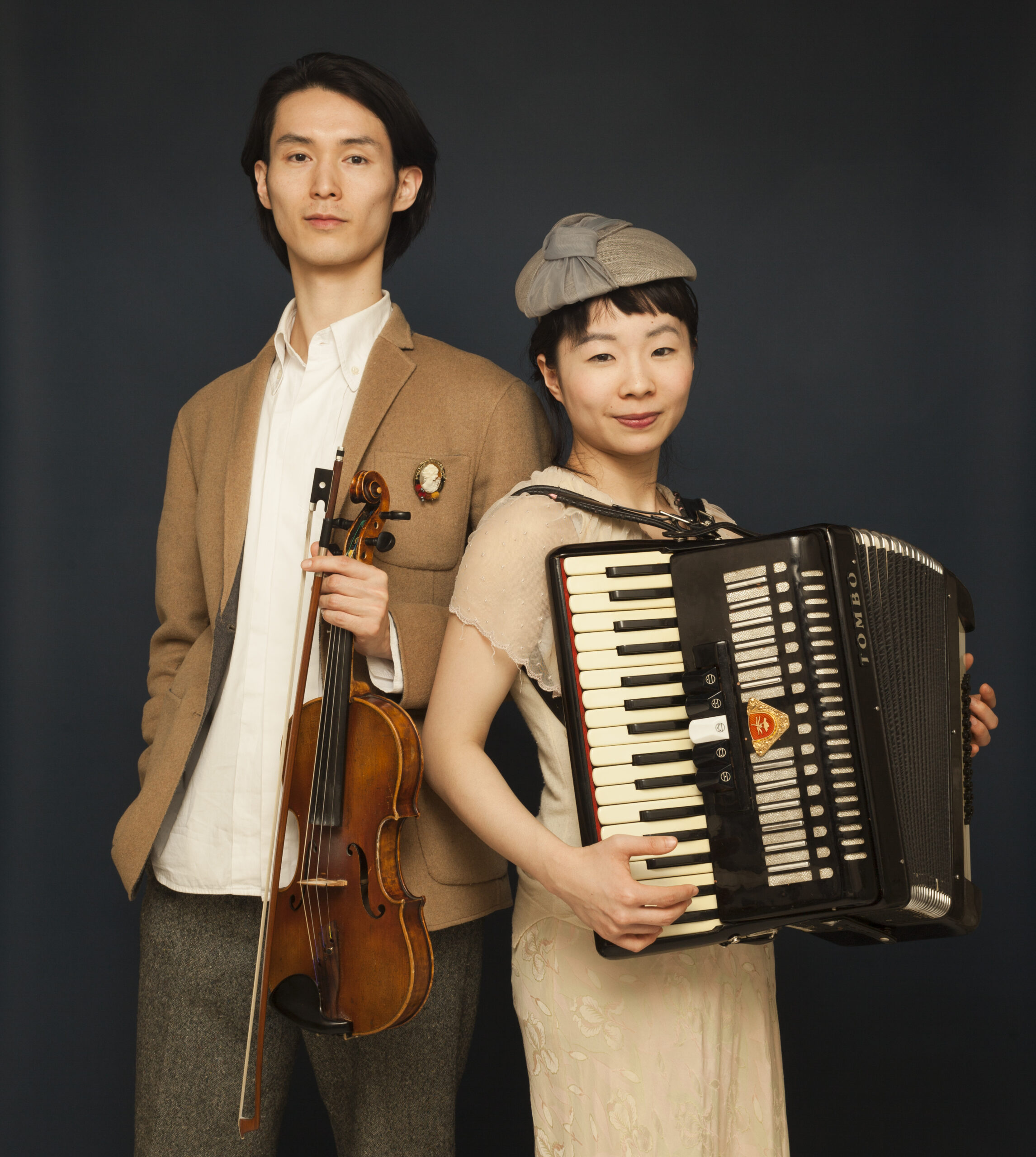 神奈川県あそび歌プロジェクト「世界の歌とあそぼう」音楽家の3日満月（権頭真由さん、佐藤公哉さん）のアーティスト写真。権頭さんはアコーディオンを、佐藤さんはバイオリンを持っている。