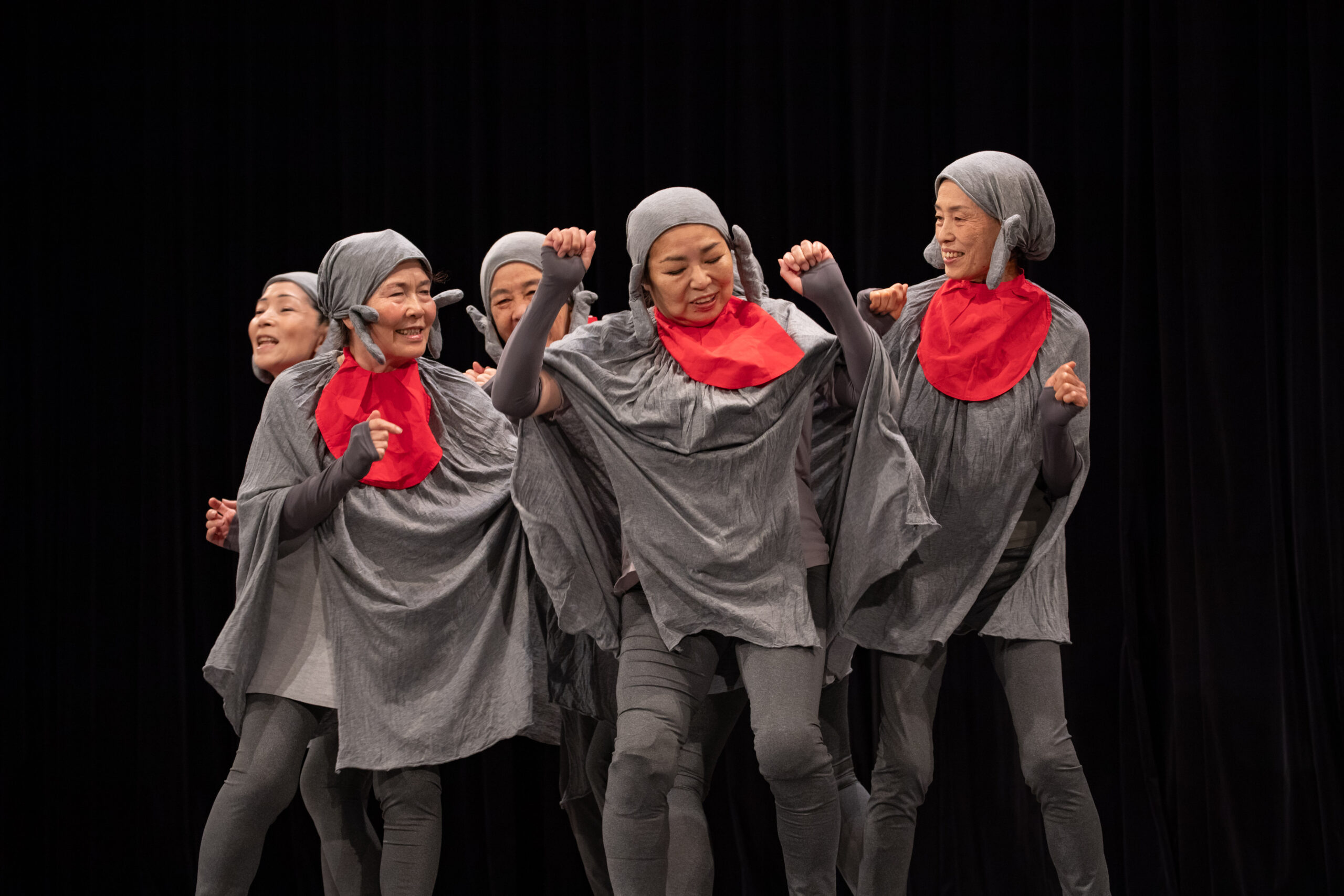 横須賀シニア劇団第6回公演「かさじぞう」の公演写真。6名のかさじぞうたちが寄り集まっている。中には両手をあげて踊っているようなものもいる。