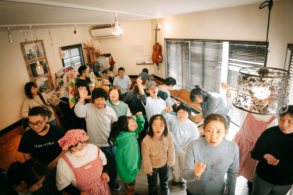 「Live Cafe Music of Mind」で披露された「ふぇありーないん」の音楽パフォーマンス。15名ほどのメンバーが、それぞれ歌ったり、踊ったり、ギターやピアノなどの楽器を演奏している様子が写っている。