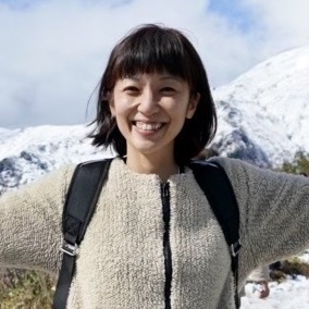 中村マミコさんの写真。山を背景に両手を広げている。