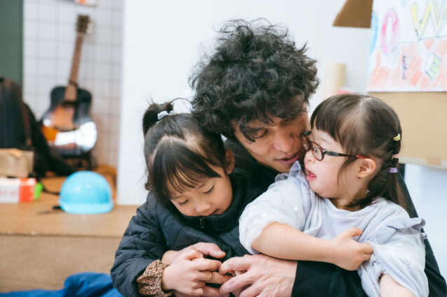 「えんげきのがっこう」で、子どもたちを両脇に抱きかかえる加藤さんの写真。