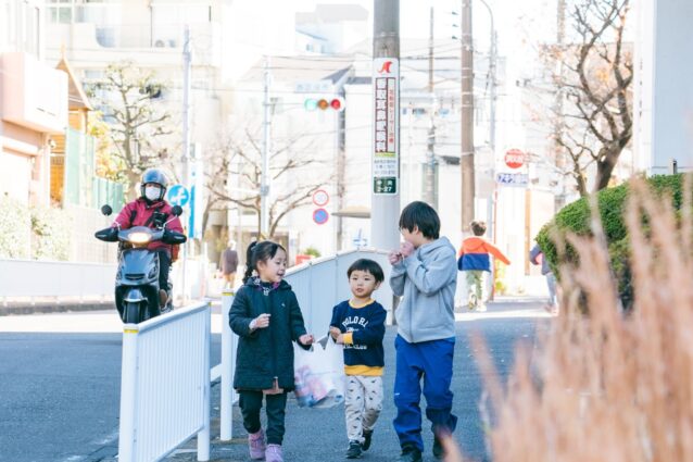 取材当日、昼ご飯を買いに出かけ、studio oowaに戻る子どもたちの様子。帰り道、3人の子どもが横に並んで歩いている。そのうち2人が買い物袋を一緒に提げている。